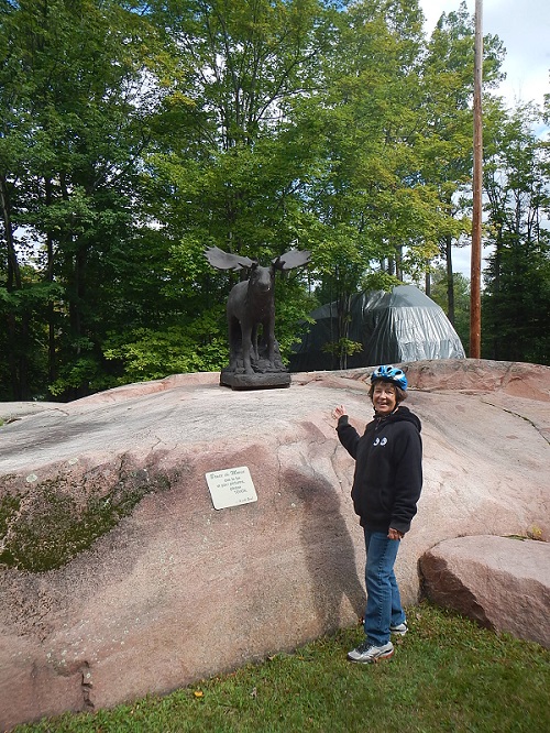 2017 Kathy poses with Bruce the Moose encountered on our
        bike ride